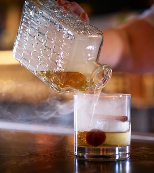 A server preparing a cocktail with a cherry, smokey whiskey at Yellowbell