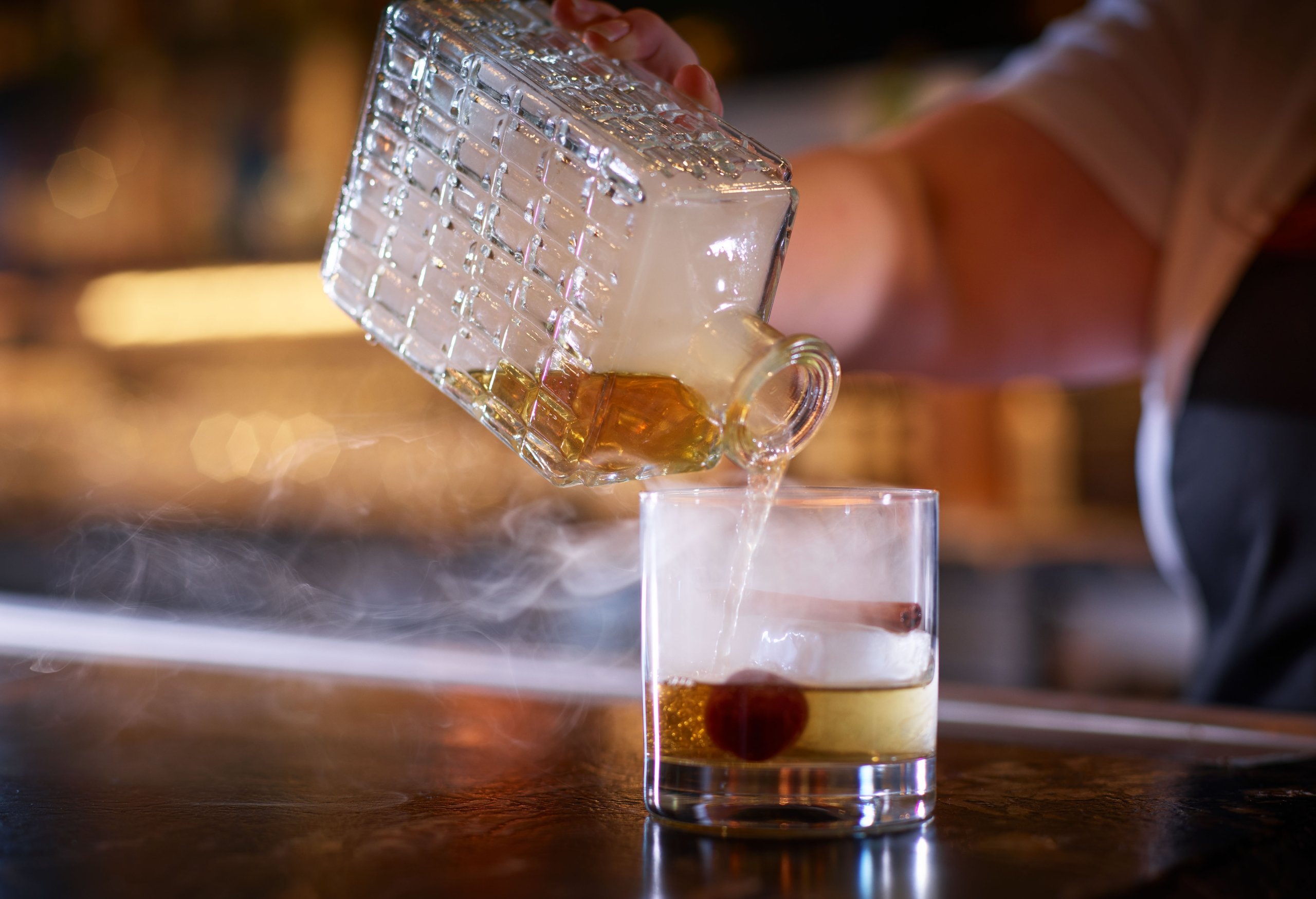 A server preparing a cocktail with a cherry, smokey whiskey at Yellowbell