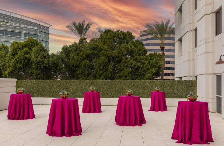 Outdoor space at sunset at the Camby with 6 round standing tables covered in pink table cloths