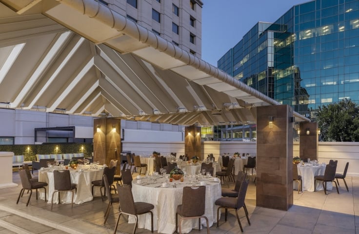 An outdoor gathering space at the Camby with several large round tables setup for an event