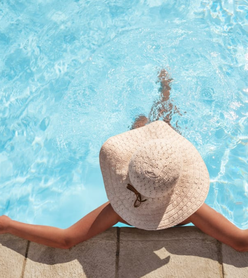 A woman wearing a sun hat, sitting in the rooftop pool at the Camby