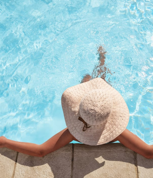 A woman wearing a sun hat, sitting in the rooftop pool at the Camby