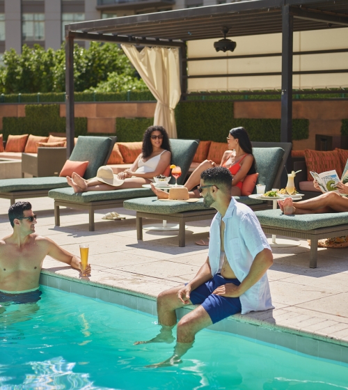 3 women lounging and 2 men hanging poolside at the Camby