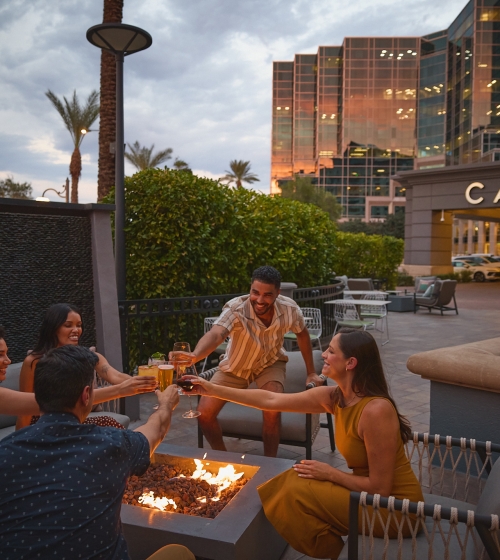 Men and women socializing over a firepit. Drinking, cheers, Yellowbell patio