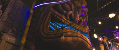 A close-up view of a large, illuminated statue with colorful lights and hanging bulbs at night.
