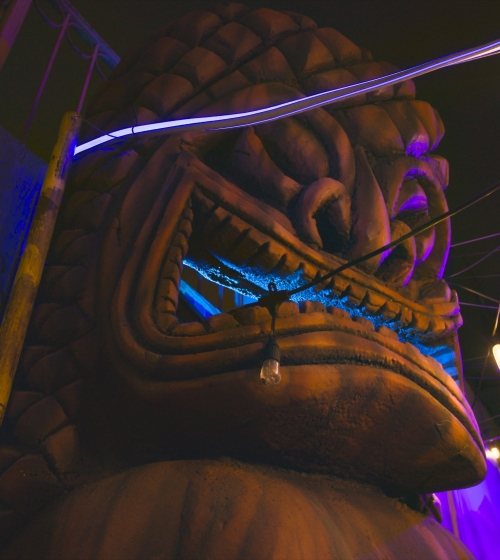 A close-up view of a large, illuminated statue with colorful lights and hanging bulbs at night.