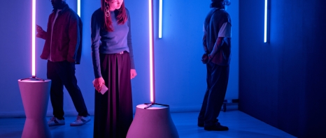 Individuals observing light sculptures in modern art gallery with neon blue and pink lighting creating an immersive, thoughtful environment