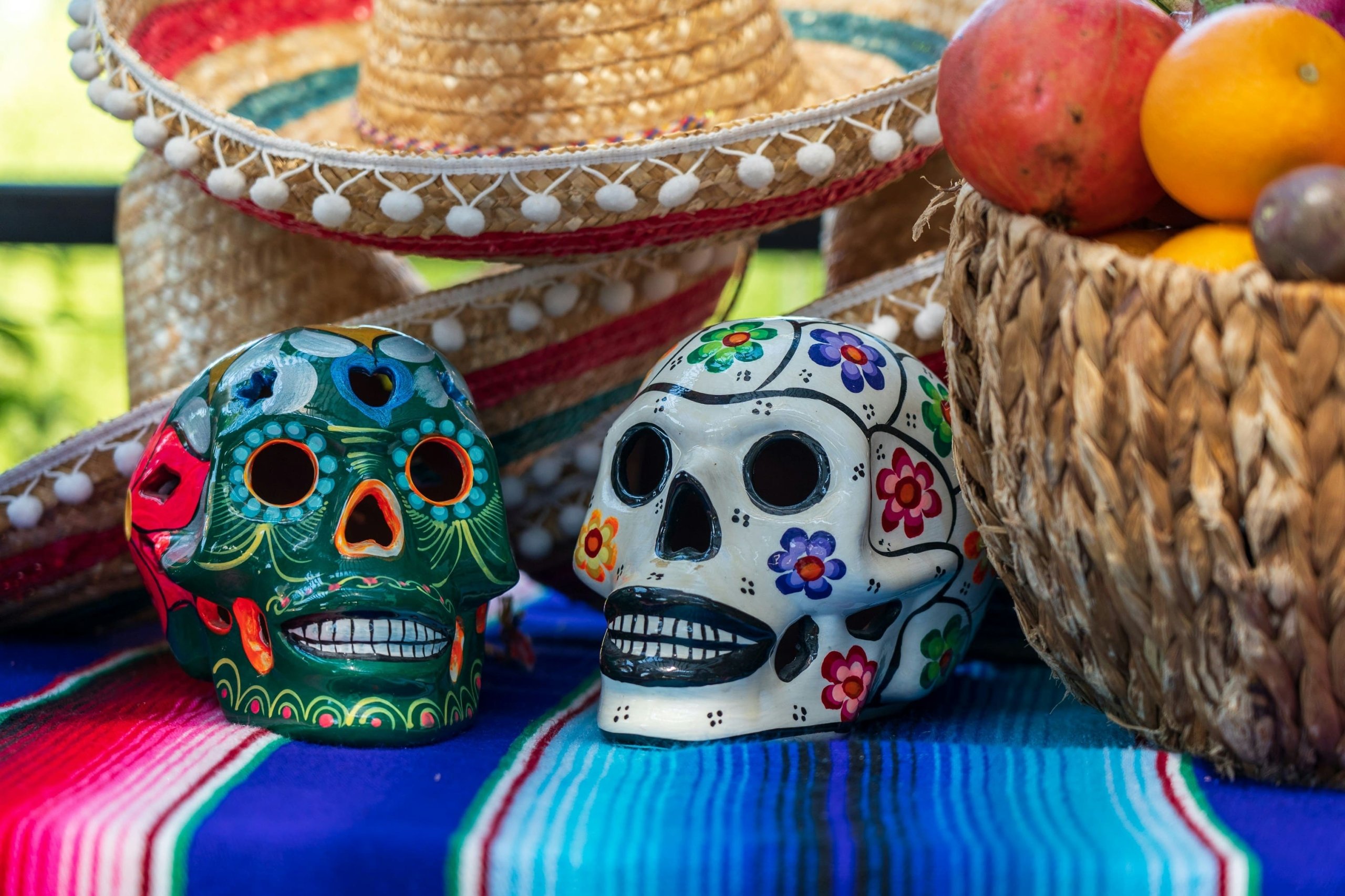 Dia De Los Muertos. Two skulls, sombrero, basket of fruit, red and blue blanket.