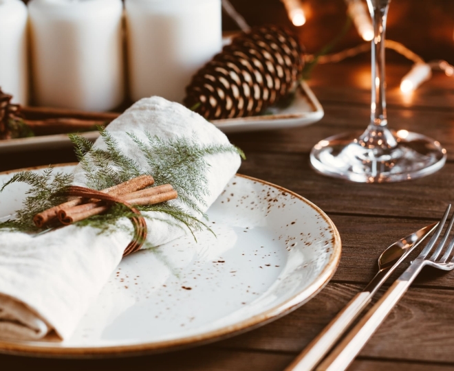 Christmas table setting with white plate, white napkin, cinnamon sticks, candles